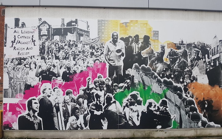 A mural commemorating the Battle of Lewisham with black and white photography from the day including a banner and Darcus Howe.