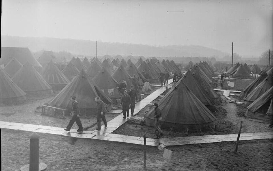 Black-and-white photograph of a prisoner of war camp with rows of tents and individuals walking along wooden paths.